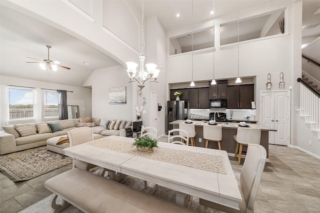 dining area featuring ceiling fan with notable chandelier, arched walkways, baseboards, a towering ceiling, and stairs