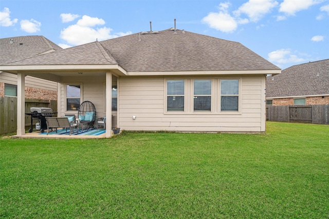 rear view of house featuring a patio area, a lawn, a shingled roof, and a fenced backyard