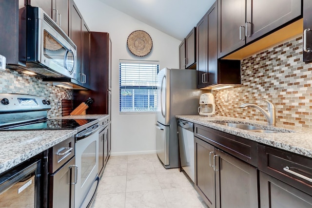 kitchen featuring dark brown cabinetry, sink, vaulted ceiling, stainless steel appliances, and light stone countertops