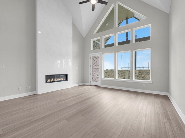 29651 Bur Creek Ln, Fulshear, TX 77441 - unfurnished living room with wood finished floors, ceiling fan, a large fireplace, high vaulted ceiling, and baseboards