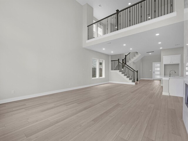 29651 Bur Creek Ln, Fulshear, TX 77441 - unfurnished living room featuring stairway, light wood-type flooring, baseboards, a sink, and a high ceiling