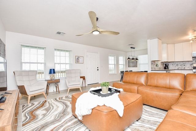 living room featuring sink, light hardwood / wood-style flooring, a healthy amount of sunlight, and ceiling fan