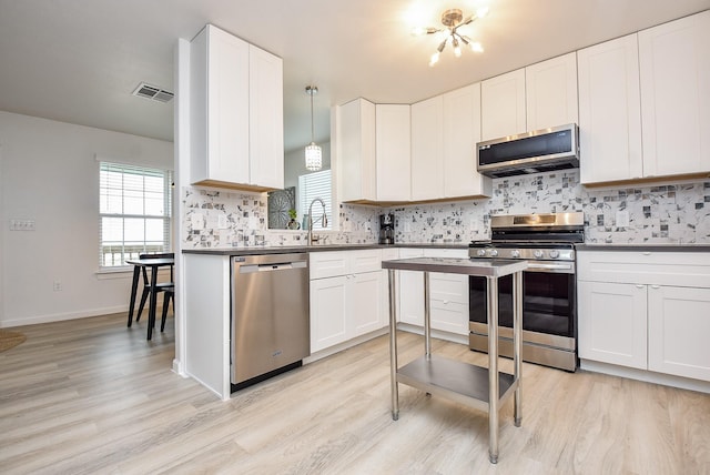 kitchen featuring tasteful backsplash, decorative light fixtures, light wood-type flooring, stainless steel appliances, and white cabinets