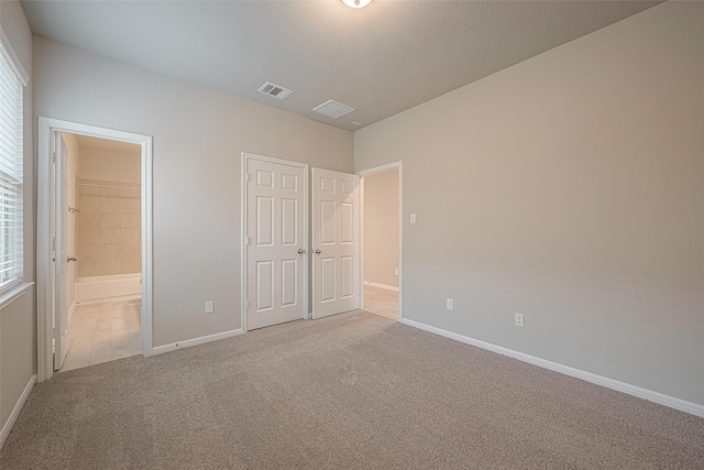 unfurnished bedroom with light carpet, ensuite bath, and a closet