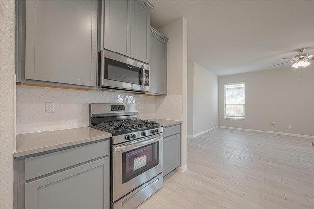 kitchen with ceiling fan, appliances with stainless steel finishes, gray cabinetry, backsplash, and light hardwood / wood-style floors