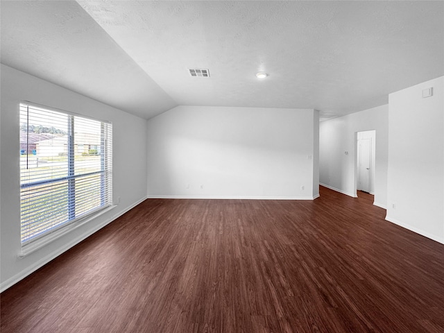 empty room featuring vaulted ceiling, dark wood-type flooring, visible vents, and baseboards