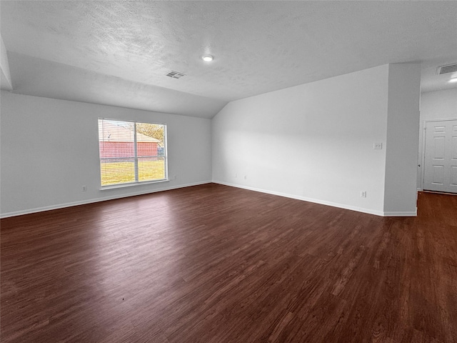 empty room featuring baseboards, visible vents, lofted ceiling, dark wood-type flooring, and a textured ceiling