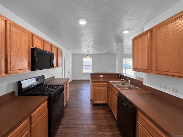 kitchen featuring brown cabinets, dark wood finished floors, dark countertops, a sink, and black appliances