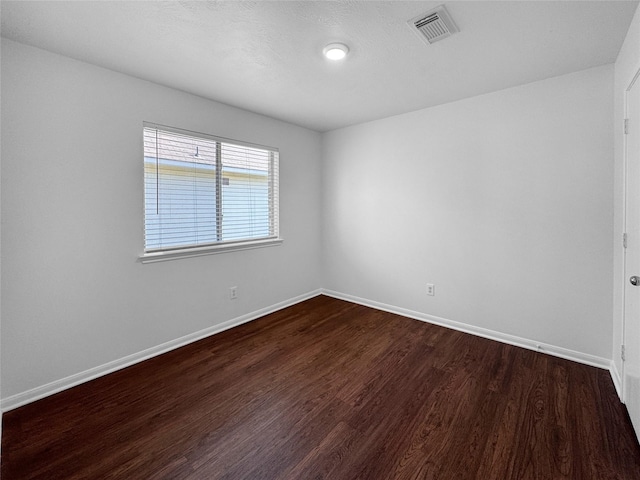 unfurnished room featuring dark wood-type flooring, visible vents, and baseboards