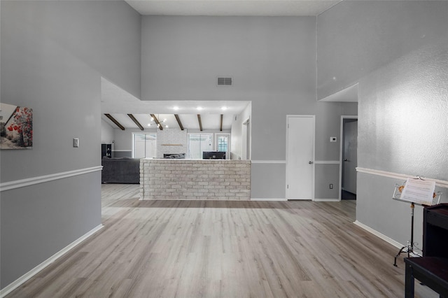 unfurnished living room with beam ceiling, a high ceiling, and light wood-type flooring