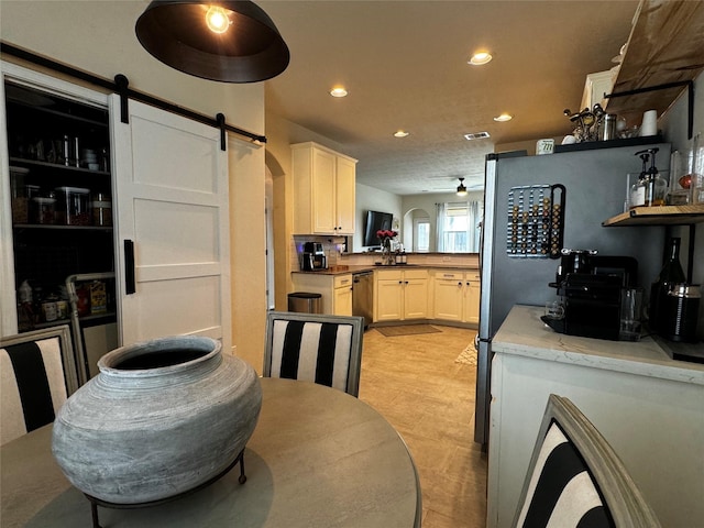 kitchen featuring ceiling fan, stainless steel dishwasher, a barn door, and white cabinets