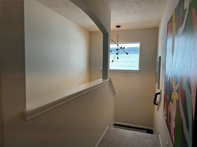 staircase featuring an inviting chandelier and a textured ceiling