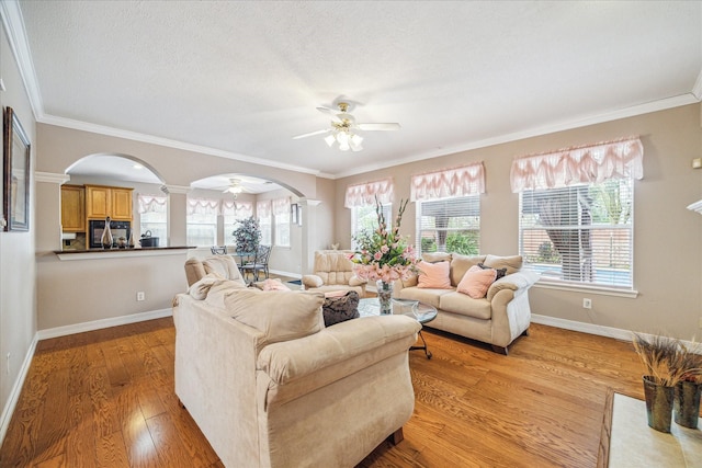 living room with light hardwood / wood-style flooring, a textured ceiling, ceiling fan, crown molding, and decorative columns