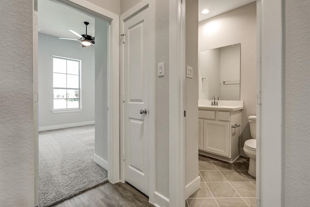 half bath with baseboards, toilet, a textured wall, vanity, and a ceiling fan