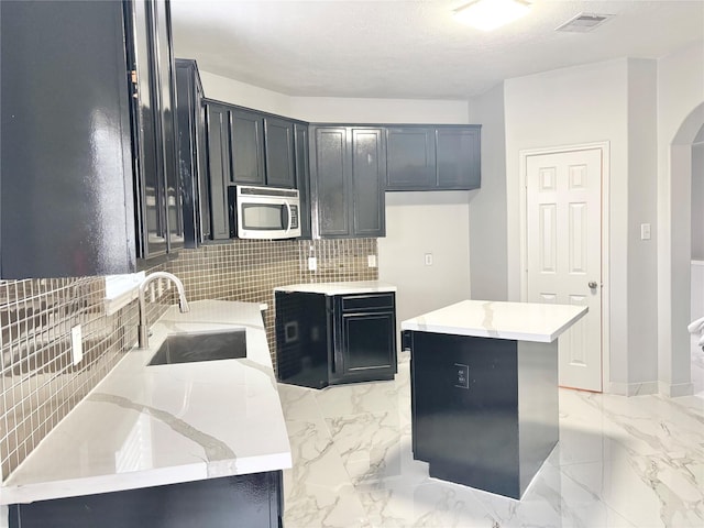 kitchen with tasteful backsplash, light stone countertops, a center island, and sink