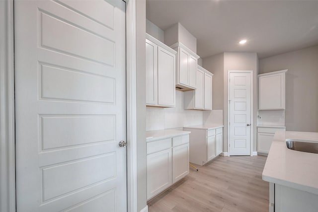 kitchen featuring recessed lighting, backsplash, white cabinetry, a sink, and light wood-type flooring