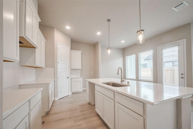 kitchen featuring a center island with sink, visible vents, light wood-style flooring, decorative backsplash, and a sink