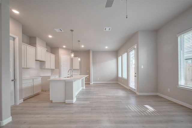 kitchen with light wood finished floors, a center island with sink, a sink, and visible vents