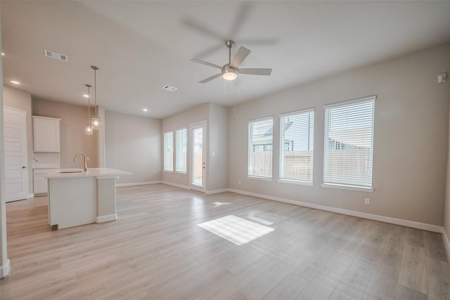 unfurnished living room with light wood-style floors, baseboards, visible vents, and a sink