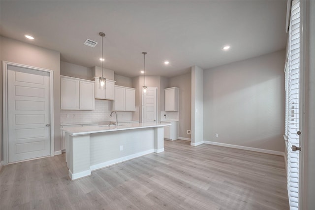 kitchen featuring a center island with sink, light wood finished floors, tasteful backsplash, visible vents, and a sink