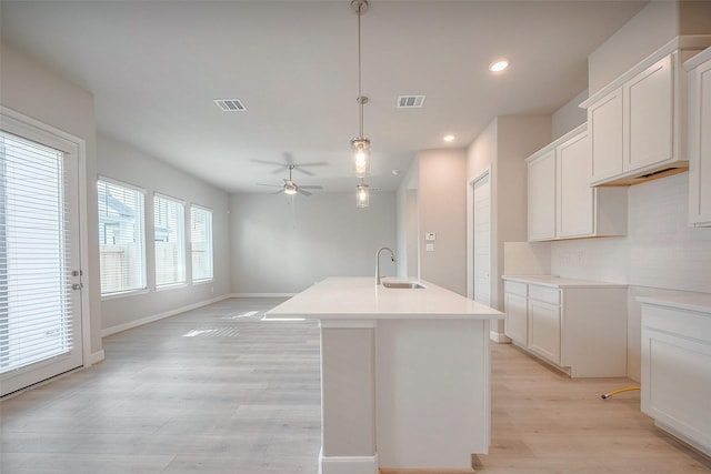 kitchen featuring a sink, visible vents, light wood-type flooring, decorative backsplash, and a center island with sink