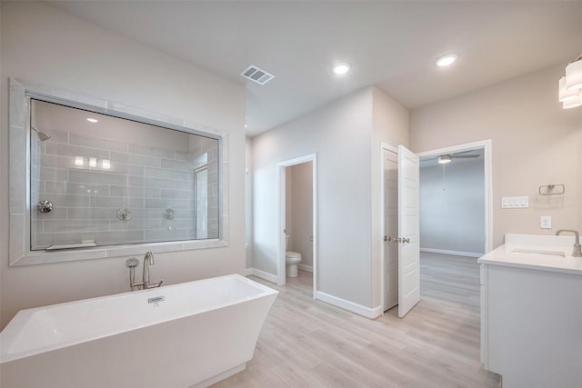 bathroom featuring baseboards, visible vents, toilet, wood finished floors, and a freestanding tub