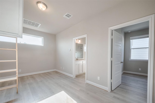 unfurnished bedroom with light wood-type flooring, visible vents, a sink, and baseboards