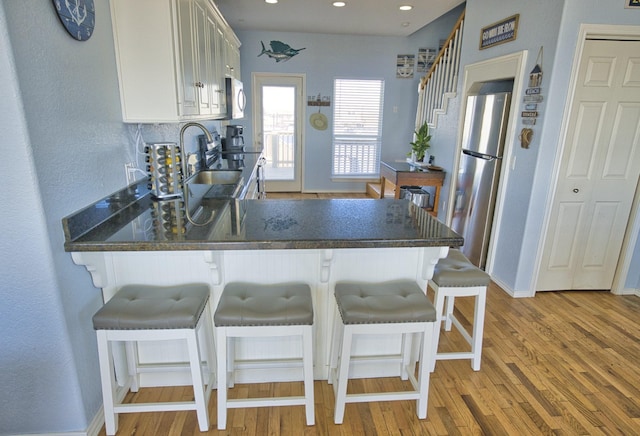 kitchen featuring appliances with stainless steel finishes, a breakfast bar area, white cabinets, kitchen peninsula, and light wood-type flooring