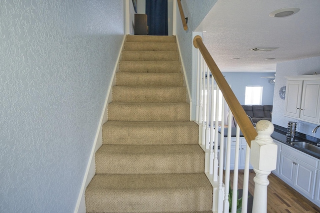 staircase featuring sink, hardwood / wood-style flooring, and a textured ceiling