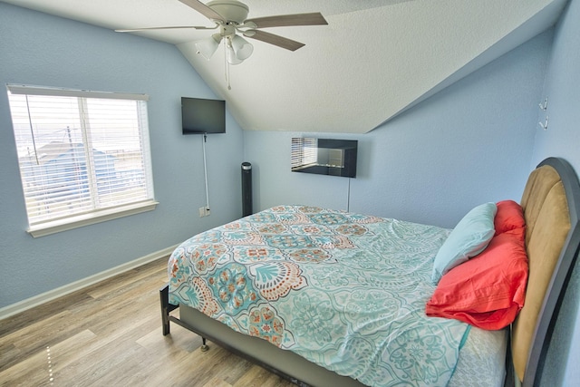 bedroom featuring vaulted ceiling, a wall mounted AC, ceiling fan, a textured ceiling, and light hardwood / wood-style flooring