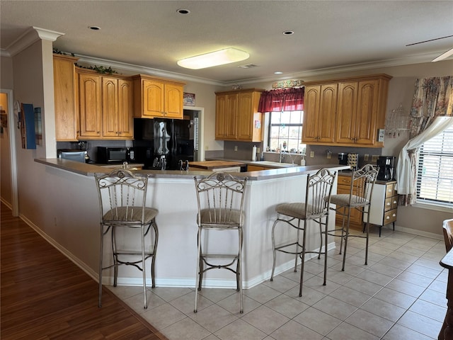 kitchen featuring ornamental molding, black appliances, kitchen peninsula, and a kitchen bar