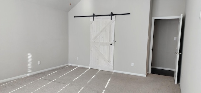 unfurnished bedroom featuring vaulted ceiling, a barn door, and light carpet