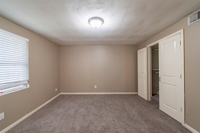 unfurnished bedroom with a textured ceiling and dark colored carpet