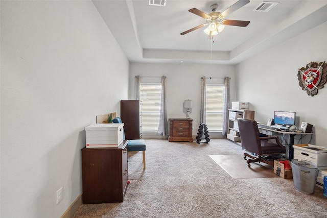 carpeted office space featuring ceiling fan and a tray ceiling