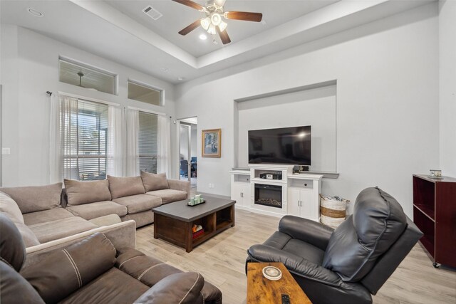 living room featuring light hardwood / wood-style flooring, a raised ceiling, and ceiling fan