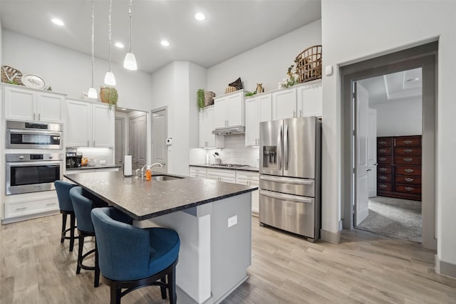 kitchen with a sink, appliances with stainless steel finishes, dark countertops, a kitchen breakfast bar, and tasteful backsplash