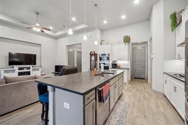 kitchen with white cabinetry, a tray ceiling, an island with sink, and light hardwood / wood-style flooring