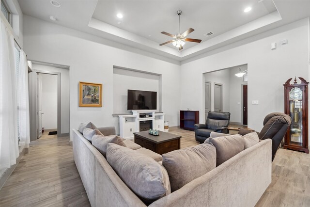 living room featuring ceiling fan, a towering ceiling, a raised ceiling, and light wood-type flooring