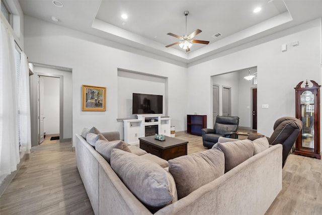 living area with visible vents, light wood-style flooring, and a raised ceiling