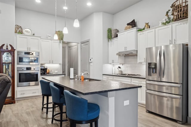 kitchen with dark countertops, backsplash, under cabinet range hood, stainless steel appliances, and a sink