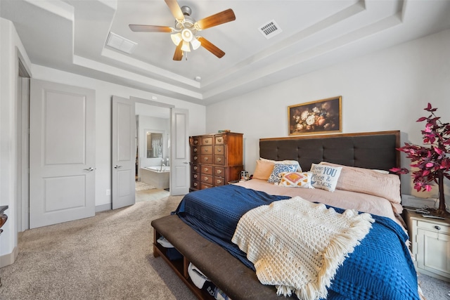 carpeted bedroom featuring a tray ceiling, ensuite bath, and ceiling fan