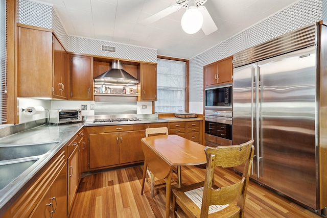 kitchen with ceiling fan, built in appliances, light hardwood / wood-style floors, and wall chimney range hood