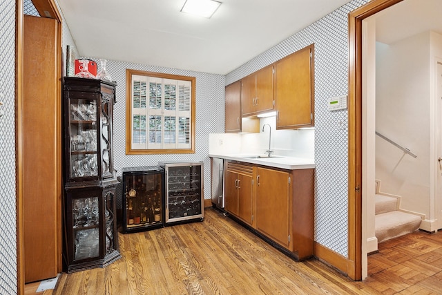 bar featuring sink, stainless steel dishwasher, wine cooler, and light wood-type flooring