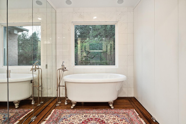 bathroom with tile walls, a tub to relax in, and wood-type flooring