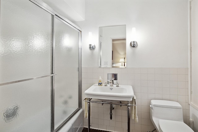 full bathroom with tile walls, sink, combined bath / shower with glass door, and toilet