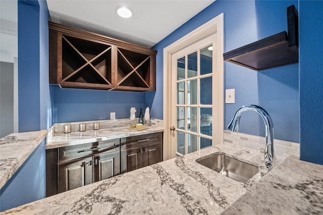 kitchen featuring light stone counters, sink, dark brown cabinets, and range hood