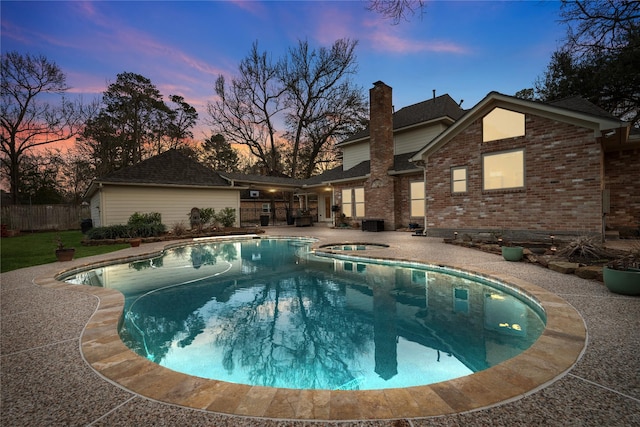 pool at dusk with an in ground hot tub and a patio