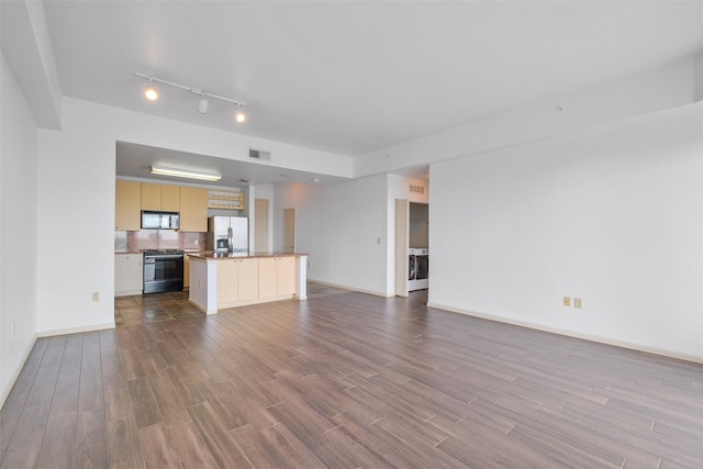 unfurnished living room featuring washer / dryer, hardwood / wood-style floors, and track lighting