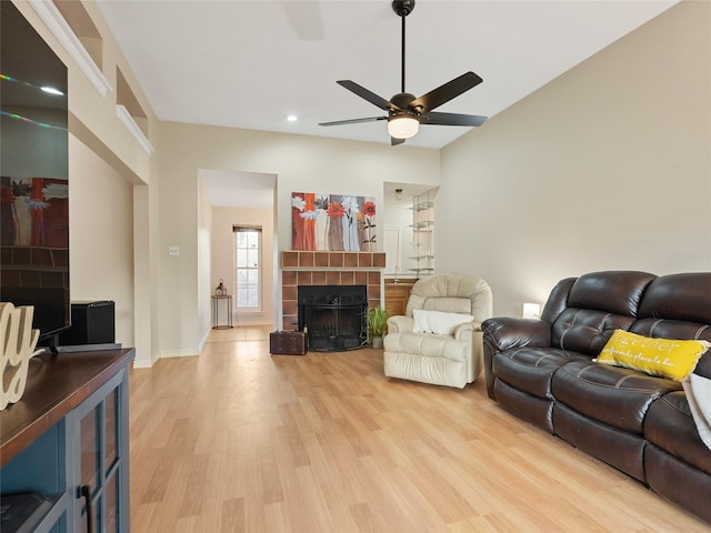 living room featuring a tiled fireplace, light wood-style flooring, baseboards, and ceiling fan