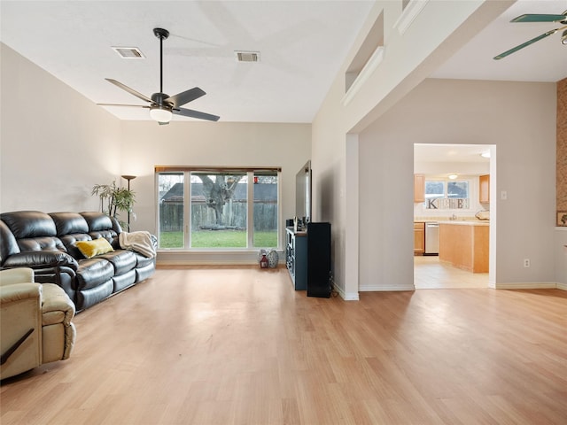 living room featuring ceiling fan, light hardwood / wood-style floors, and a towering ceiling